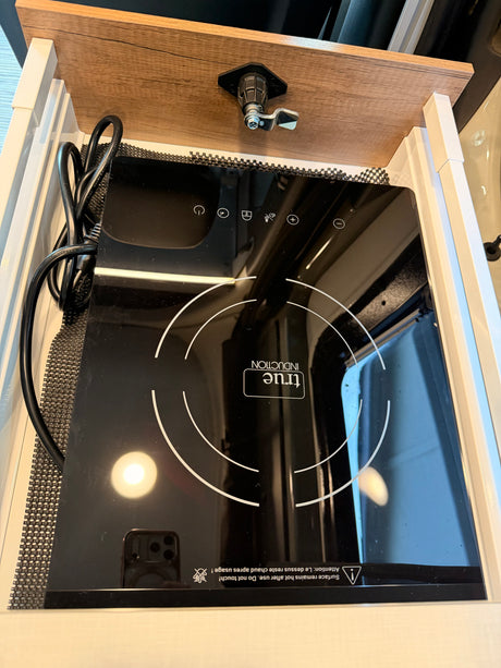This RV rental's kitchen includes a black 'true Induction' portable cooktop, neatly stored in a slide-out compartment, ready for use.