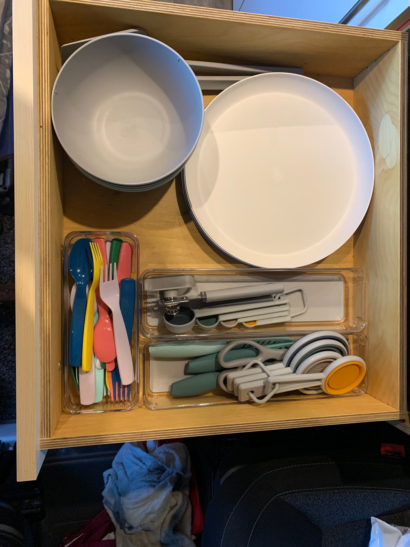 Well-organized RV rental drawer showing compact kitchenware: plates, bowls, bright cutlery, can opener, and measuring tools.