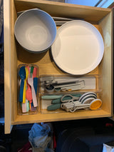 Well-organized RV rental drawer showing compact kitchenware: plates, bowls, bright cutlery, can opener, and measuring tools.