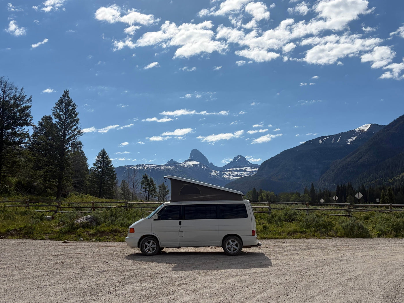 White pop-top camper van rv rental parked with iconic, snow-capped Grand Teton mountains and pine trees in the background. — photo 9