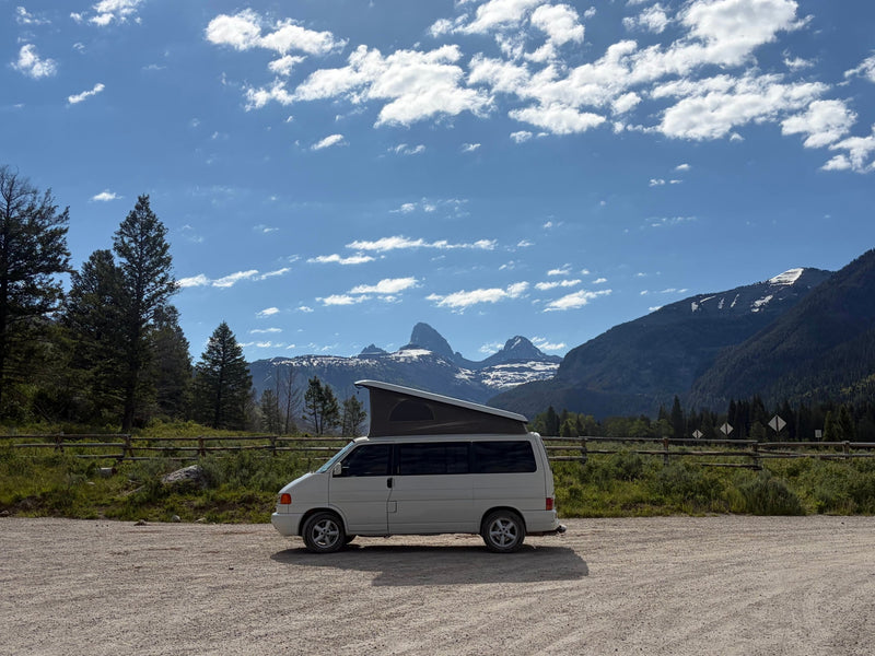 White pop-top camper van rv rental parked with iconic, snow-capped Grand Teton mountains and pine trees in the background. — photo 9