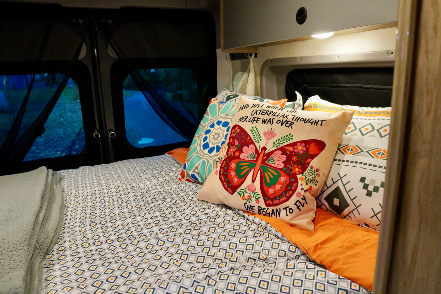 Cozy RV rental bedroom featuring a bed with patterned bedding, a butterfly pillow, and night views outside.