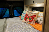 Cozy RV rental bedroom featuring a bed with patterned bedding, a butterfly pillow, and night views outside.
