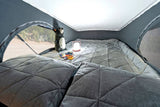 Cozy pop-top RV rental bed with a view, comfy pillows, a stuffed animal, and a light for evening reading.