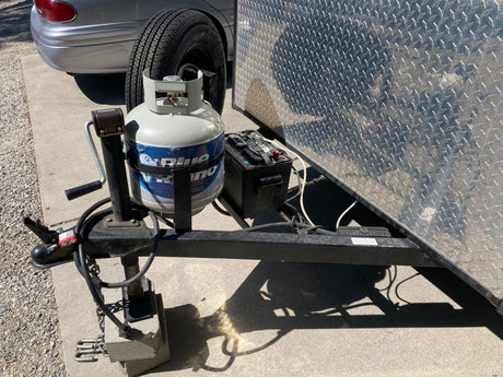 Essential components for an RV rental trip: A trailer's hitch, propane tank, and battery, ready for towing.