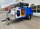Vibrant blue & white teardrop trailer RV rental with rooftop tent and open door revealing wood interior. Ready for your next camping adventure!