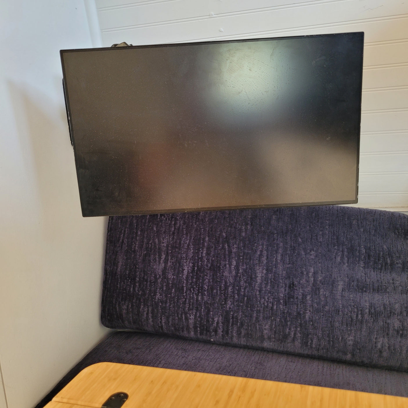Dusty TV above a textured purple dinette cushion and wooden table in an RV rental.