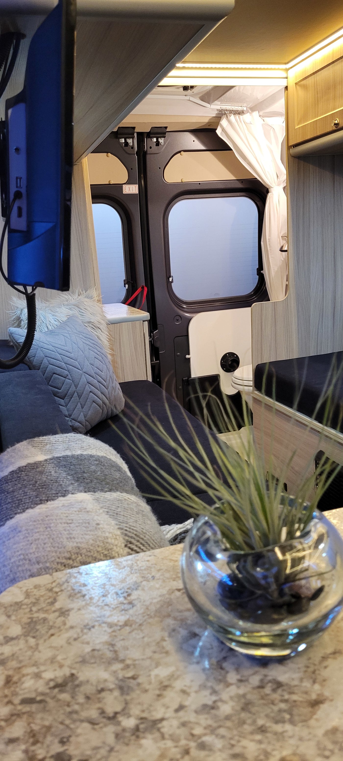 Inside a comfy RV rental: view of bed, TV, rear "EXIT" doors, and a shower area. Perfect for van life adventures. — photo 16