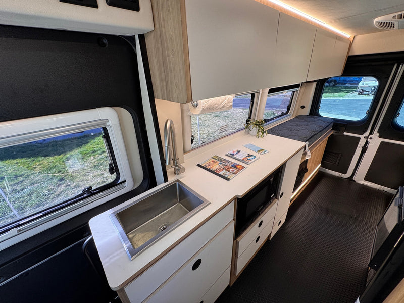 This rv rental features a modern camper van interior with a kitchenette, sink, microwave, and comfortable sleeping area. — photo 14