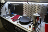 Enjoy home comforts in this RV rental's compact kitchen. Features a sink, stove, pan, and percolator.