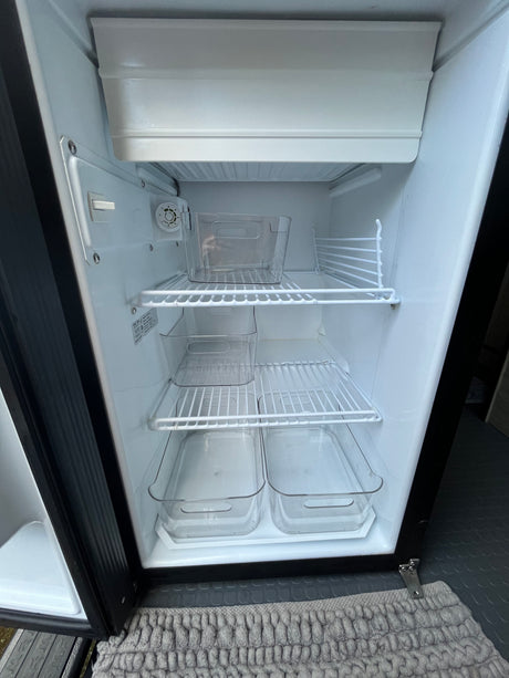 Empty, clean RV rental fridge interior. Features wire shelves, small freezer, and clear organizing bins.