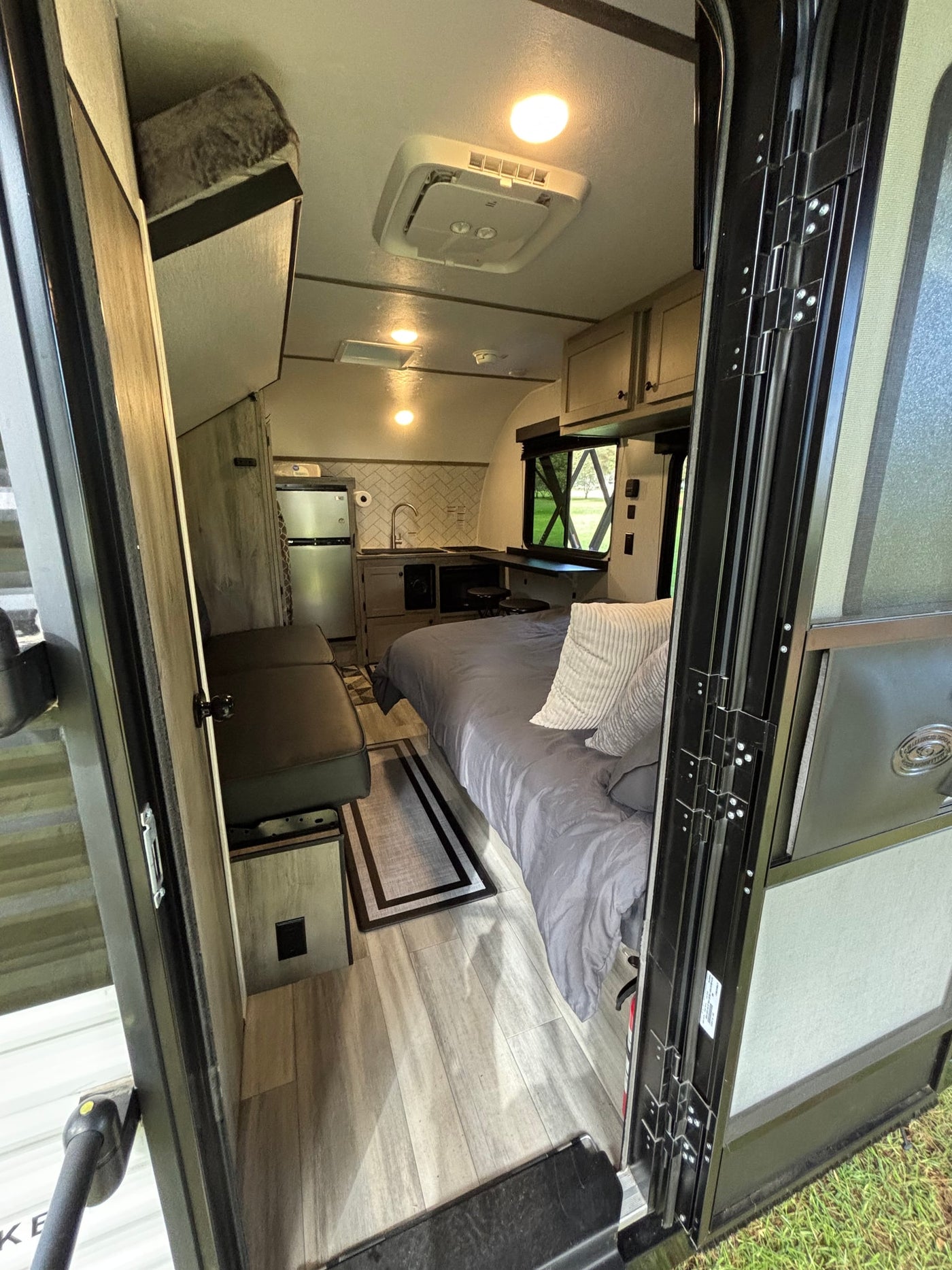 View into a compact RV rental camper, showing a cozy bed, kitchenette, dinette, and ceiling AC unit. — photo 5