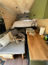 Step inside this cozy RV rental's light wood interior. Features a comfortable bed, a functional kitchen, and a lounge area.
