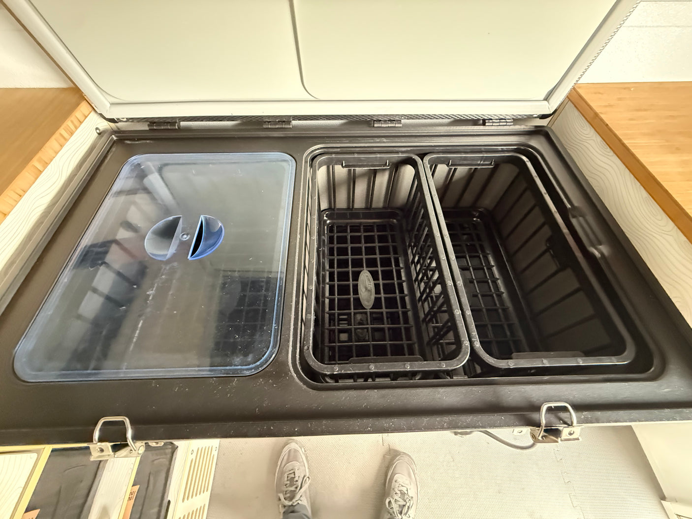 Inside an rv rental: a dual-zone portable fridge with its lid open, revealing two storage compartments, one with a clear cover.