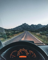 Scenic RV rental road trip: Inside view of an orange-lit dashboard and steering wheel, with the road stretching to rugged mountains.