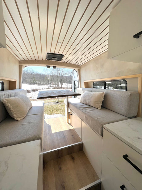 Cozy RV rental interior with comfortable seating, dining table, and scenic winter outdoor view. Ideal mobile living space.