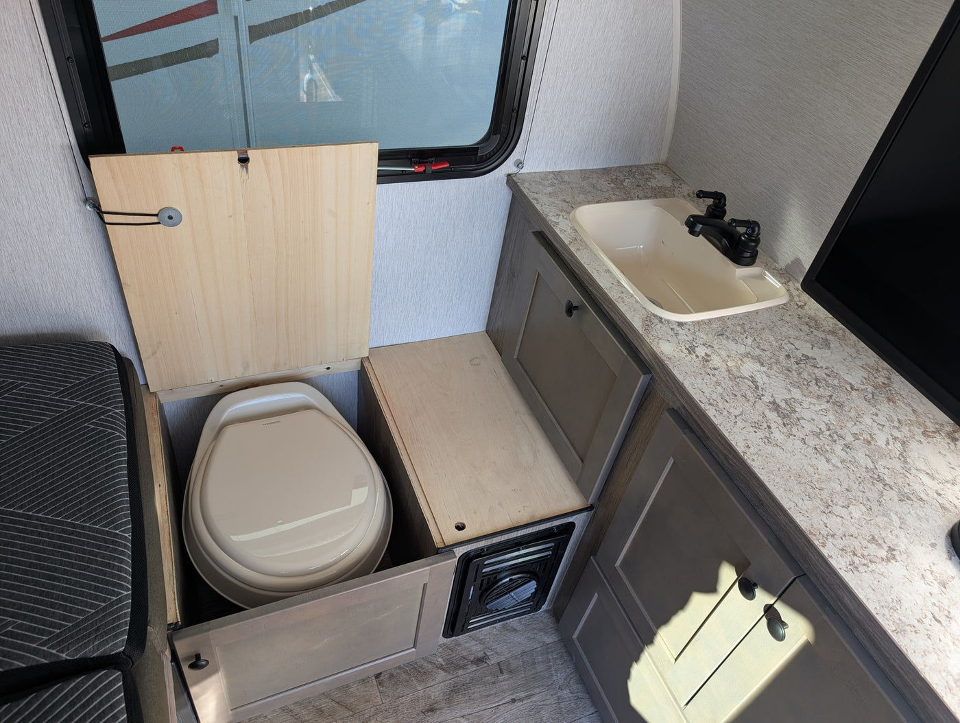 RV rental interior: clever space-saving with a Dometic toilet revealed under a hinged wooden panel, beside a sink & counter. — photo 11