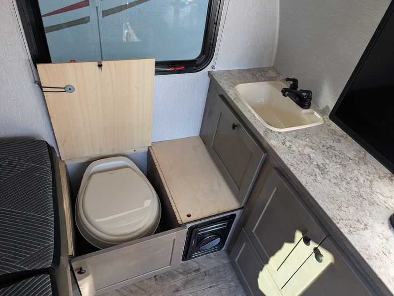 RV rental interior: clever space-saving with a Dometic toilet revealed under a hinged wooden panel, beside a sink & counter. — photo 11