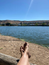 Relaxing view: bare feet propped on a log, serene lake, hills & houses. Perfect for an rv rental getaway.