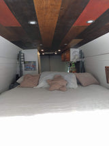 Step into this cozy RV rental camper van, featuring a comfy bed, unique wood ceiling, & smart lighting for travel.