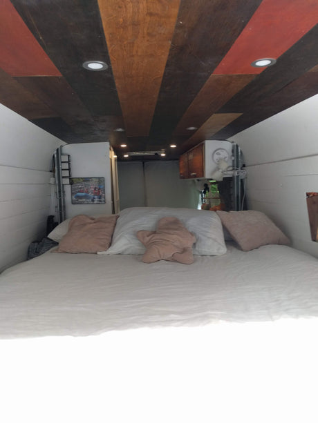 Step into this cozy RV rental camper van, featuring a comfy bed, unique wood ceiling, & smart lighting for travel.