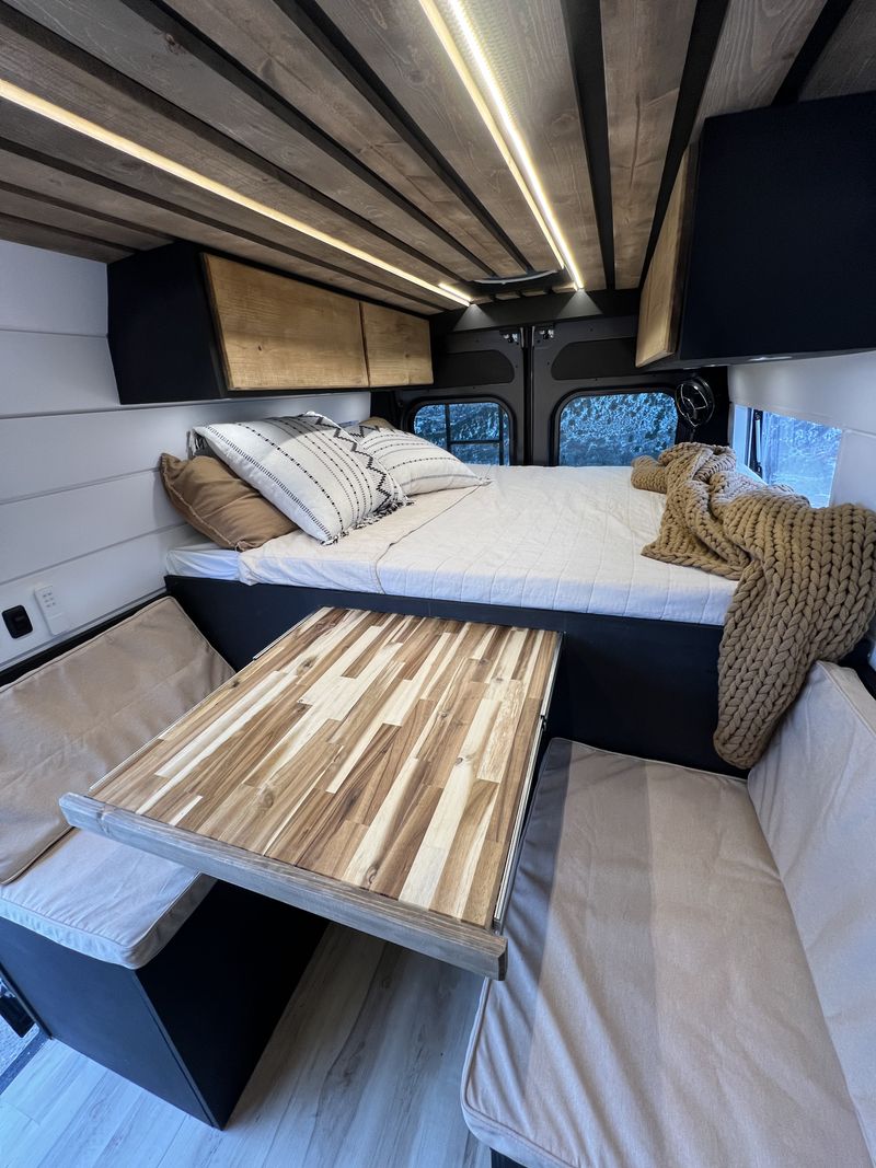  and accessible built-in fridge|Outdoor adventure: A mountain biker heads up a dirt path towards a waiting RV rental van on a hilltop under a cloudy sky.|Inside a custom RV rental: a cozy bed — photo 5