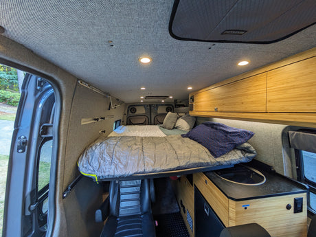 Spacious RV rental interior features a cozy elevated bed, bamboo kitchen cabinets, and functional living space.