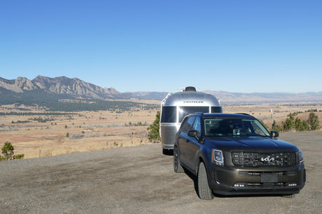 A dark SUV tows a silver Airstream RV rental on a mountain overlook with clear blue skies. Perfect for scenic trips!
