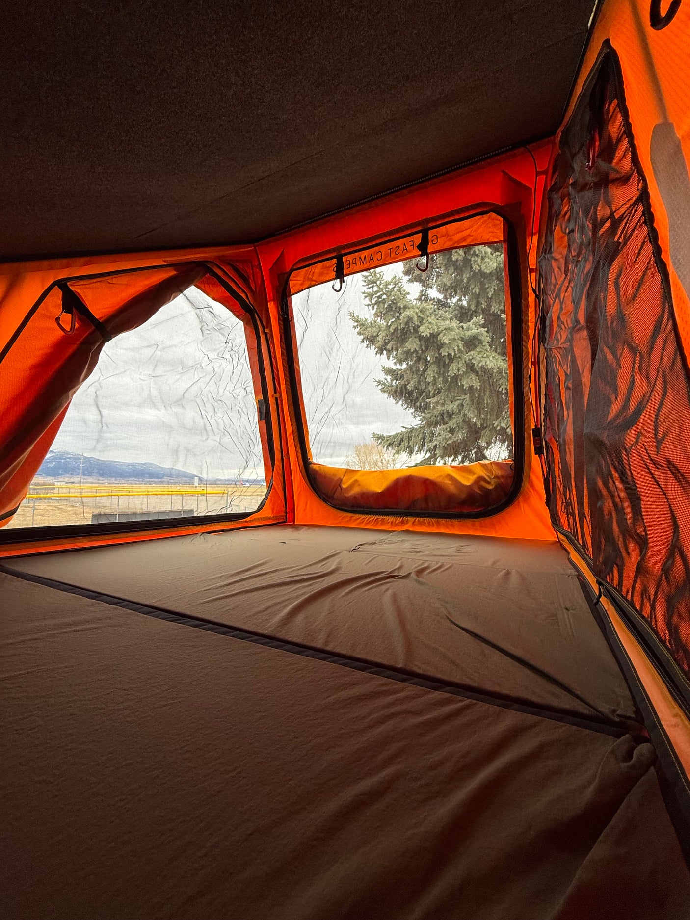 Inside a vibrant orange rooftop tent with a comfy bed & scenic mountain views. Ideal for your RV rental trip.