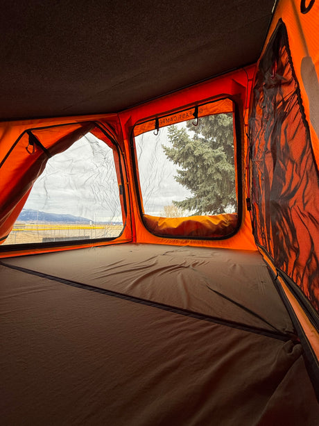Inside a vibrant orange rooftop tent with a comfy bed & scenic mountain views. Ideal for your RV rental trip.