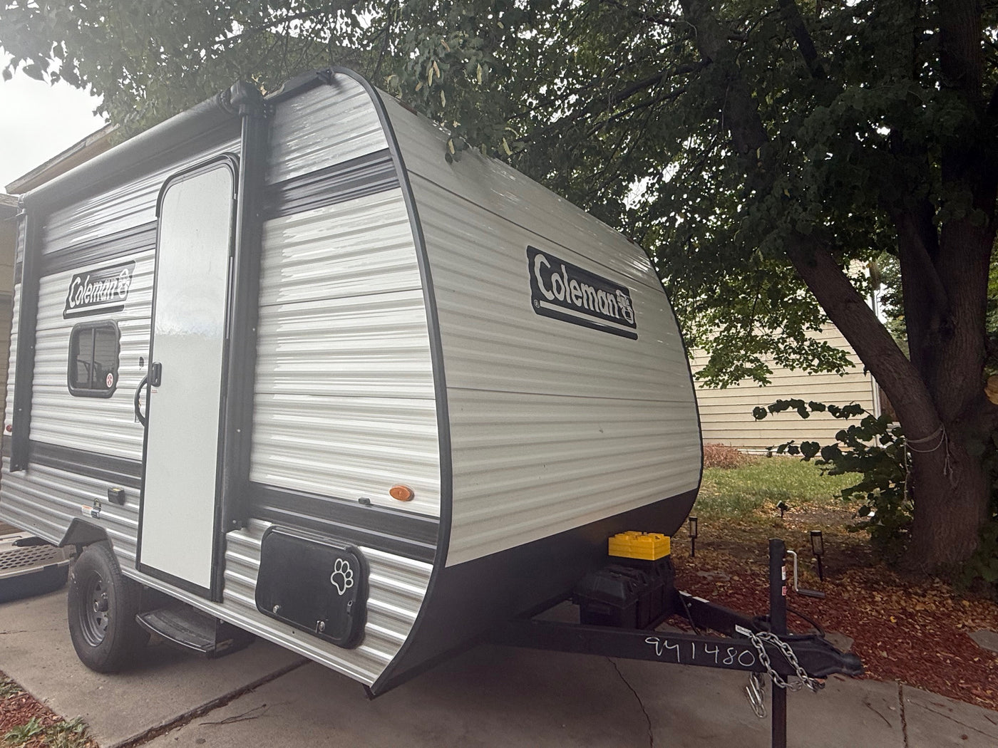 Gray Coleman travel trailer RV rental, featuring an awning, parked on a driveway under a leafy tree. — photo 8