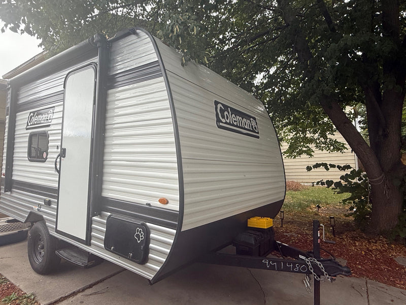 Gray Coleman travel trailer RV rental, featuring an awning, parked on a driveway under a leafy tree. — photo 8