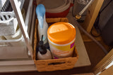 Compact cleaning supplies, including lemon scent disinfecting wipes, neatly stored in a basket under the sink in an RV rental.