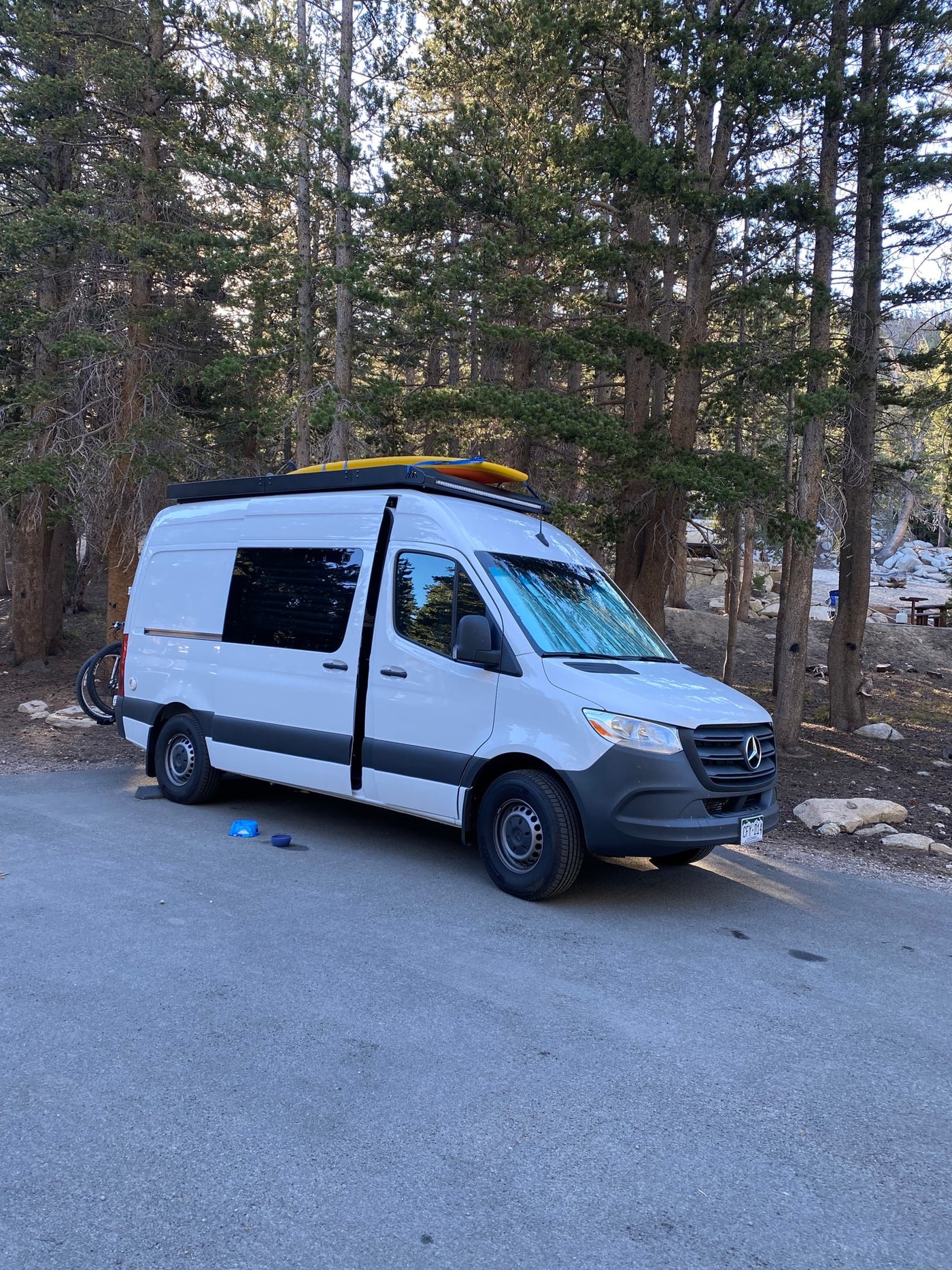 White Mercedes-Benz Sprinter RV rental parked at a scenic campground, with kayaks and a bike ready for adventure. — photo 4
