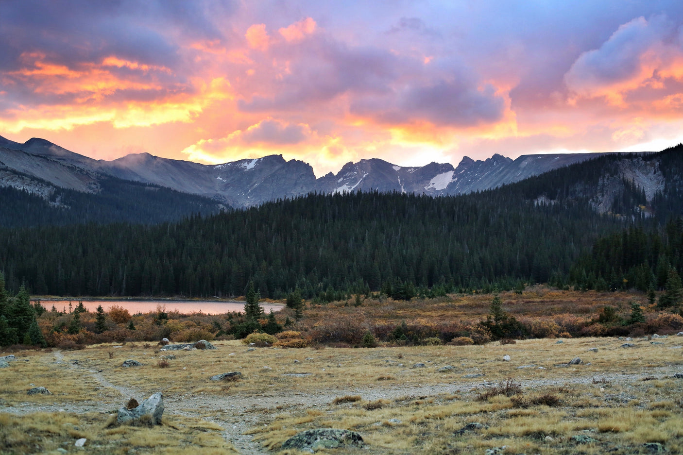 Golden & purple sunset over mountains, a tranquil lake, & pine forest. Plan your adventure with an RV rental!