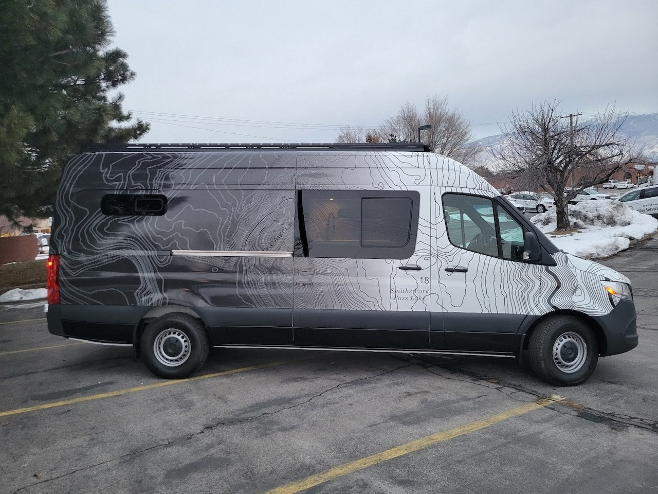 Custom Mercedes-Benz Sprinter van rv rental, featuring unique topographic map graphics, parked on an asphalt lot. — photo 8
