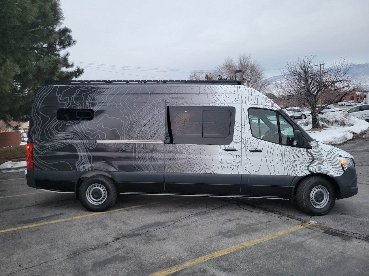 Custom Mercedes-Benz Sprinter van rv rental, featuring unique topographic map graphics, parked on an asphalt lot.