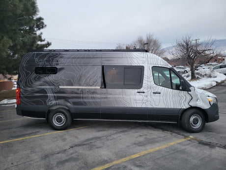 Custom Mercedes-Benz Sprinter van rv rental, featuring unique topographic map graphics, parked on an asphalt lot.