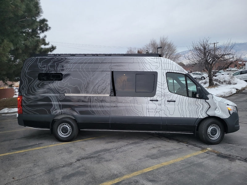 Custom Mercedes-Benz Sprinter van rv rental, featuring unique topographic map graphics, parked on an asphalt lot. — photo 8