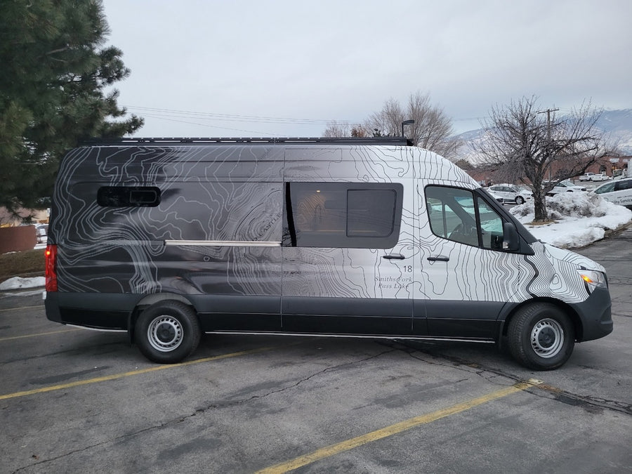 Custom Mercedes-Benz Sprinter van rv rental, featuring unique topographic map graphics, parked on an asphalt lot.