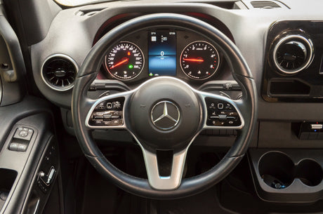 Driver's view of a Mercedes-Benz Sprinter dashboard, ideal for an RV rental. Steering wheel, digital gauges, and controls are visible.