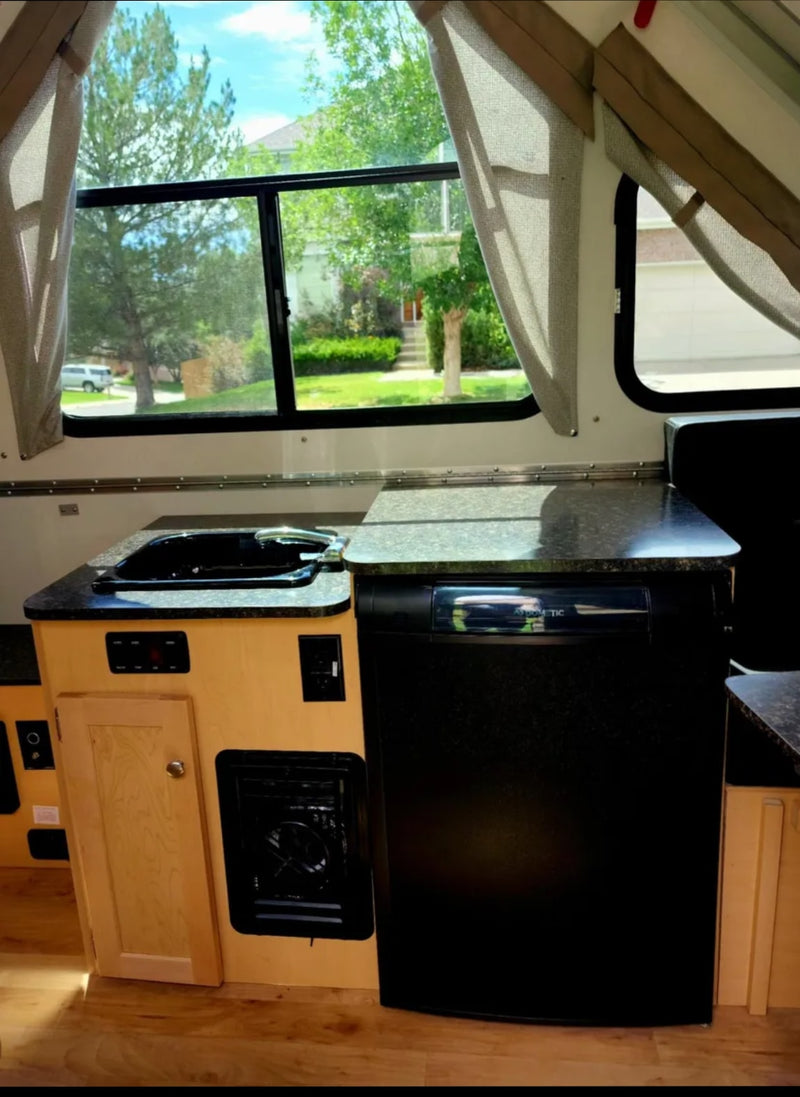  plus a dining area that converts to a bed.|RV rental: Interior of a cozy pop-up camper featuring a bed with colorful floral bedding & bright windows.|Compact RV rental kitchenette featuring a sink — photo 5