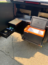 Compact outdoor kitchen from an RV rental, featuring a pull-out stove, portable fridge, and stainless steel counter.
