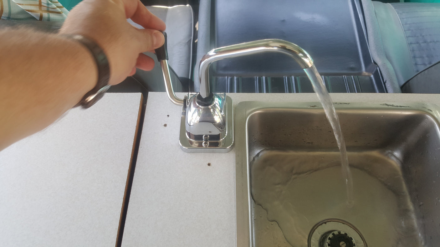 Operating the manual pump faucet in an RV rental kitchen, with fresh water flowing into the compact sink.