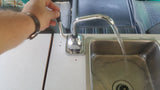 Operating the manual pump faucet in an RV rental kitchen, with fresh water flowing into the compact sink.