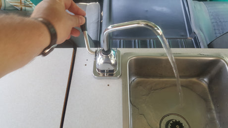 Operating the manual pump faucet in an RV rental kitchen, with fresh water flowing into the compact sink.