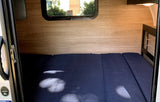 RV rental interior: A well-lit sleeping area with blue mattress, wood-grain walls, and a window, viewed from the entrance.