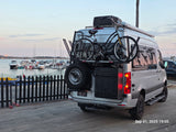 White Sprinter RV rental with bikes & spare tire at a marina. Ideal for travel & outdoor adventure.