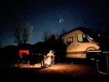 Starry night camping in an RV rental! A person sits by a glowing fire, near a modern camper van under a clear sky.