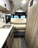 RV rental: a small camper van interior with a kitchen sink on the left, comfortable bed, and wood-toned cabinets.